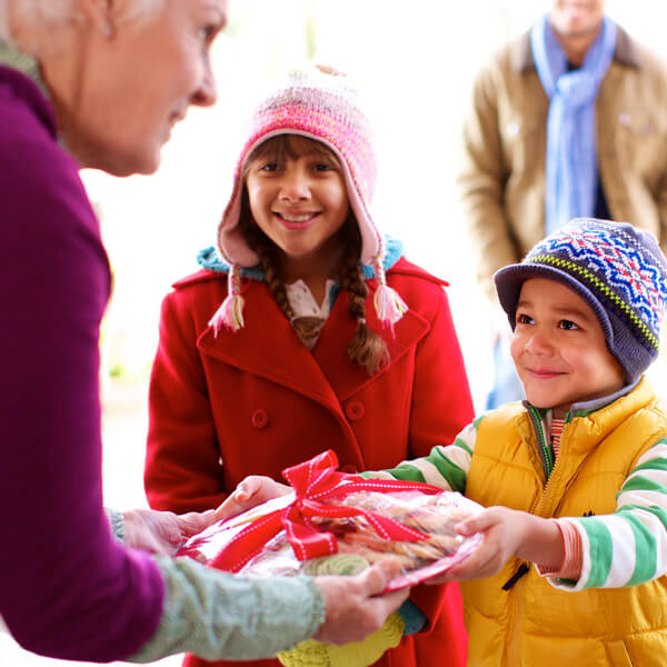 Kids giving a plate of Christmas treats to an older adult.