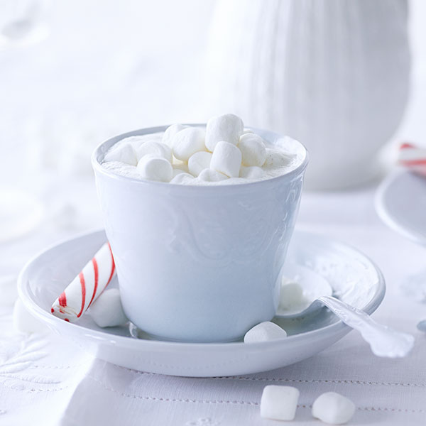 Mug of white hot chocolate with mini marshmallows on top and a candy cane on the side.