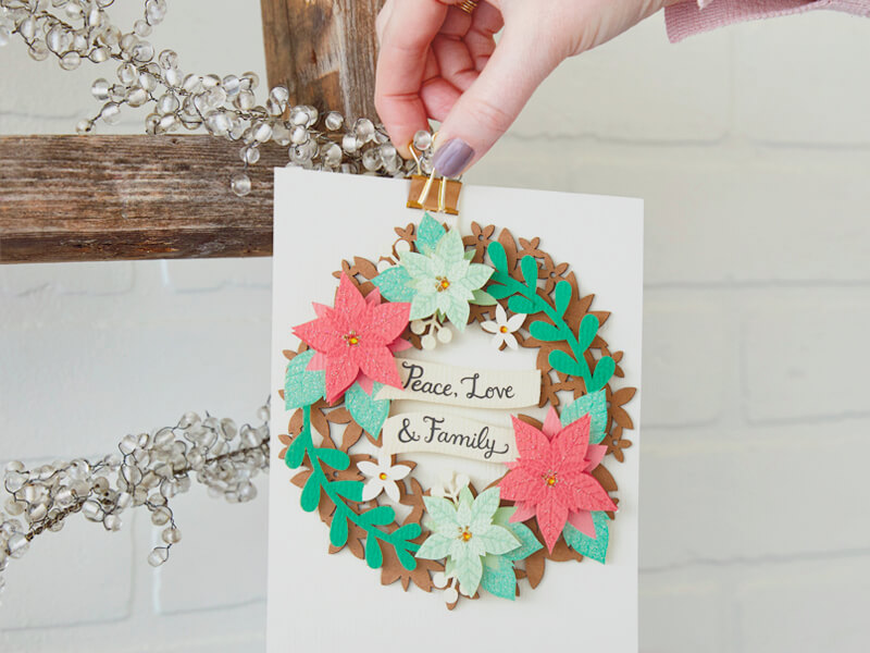 A hand clipping a card onto the wooden ladder Christmas card holder.