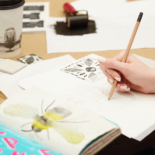A hand sketching with a stamp design with a pencil on a piece of paper.