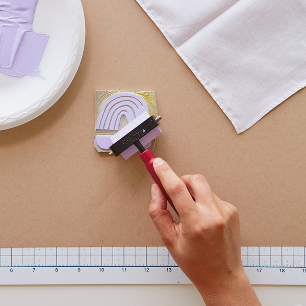 A hand applying paint to a carved rubber stamp with a roller.