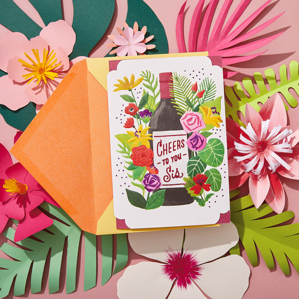 A paper craft card featuring flowers and a wine bottle that says