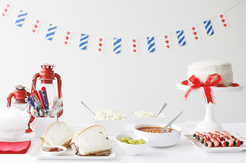 A Fourth of July food table with a red, white and blue DIY banner hung in the background.