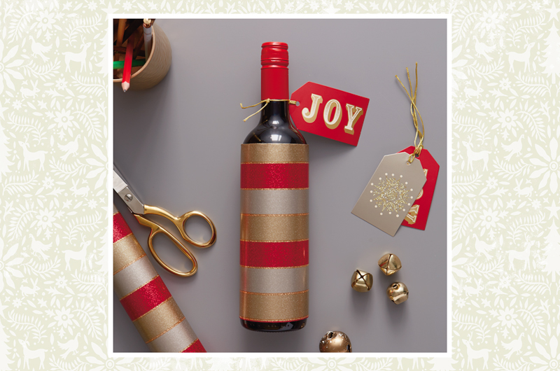A bottle of wine wrapped with gift wrap and accented with a gift tag that reads,