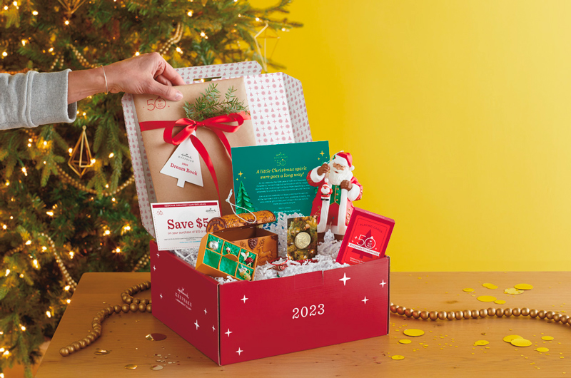 A hand opening a Keepsake Ornament Club membership box, featuring 50th anniversary messaging.