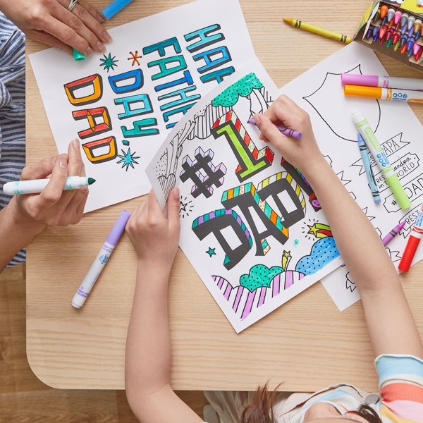 A little girl and a woman sit at a table coloring free printable Father's Day coloring pages with a variety of crayons and markers.