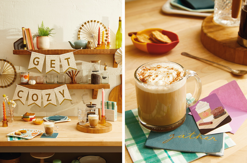 A fall drink bar is set up on a wooden countertop; the floating wooden shelves in the background have a banner hanging from them that reads,