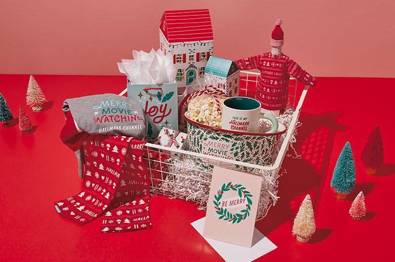 A Hallmark Channel care package that includes leggings, a long-sleeve shirt, a popcorn bowl, a mug, a wine-bottle cozy shaped like a sweater, a set of paper holiday houses, and a video card that reads,