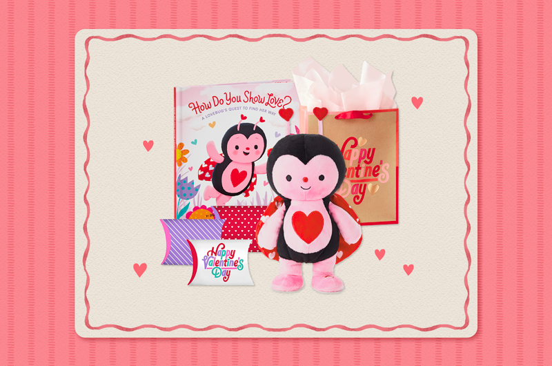 A collection of Valentine's Day gifts for a child that includes a plush, interactive ladybug that dances and sings, along with a coordinating book, a set of pillow boxes in red, purple, pink and white that are filled with treats, and a brown kraft paper gift bag with red edging that reads,