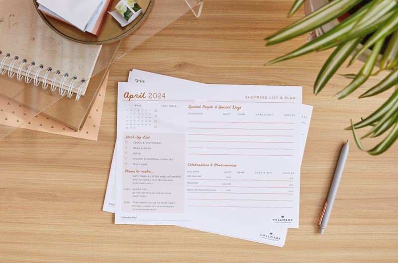 A printed April 2024 celebration planner page sitting on a home office desktop, surrounded by desk accessories.