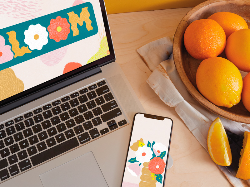 A laptop screen displaying the free June downloadable desktop wallpaper, with a mobile phone displaying the free downloadable mobile wallpaper lying nearby.