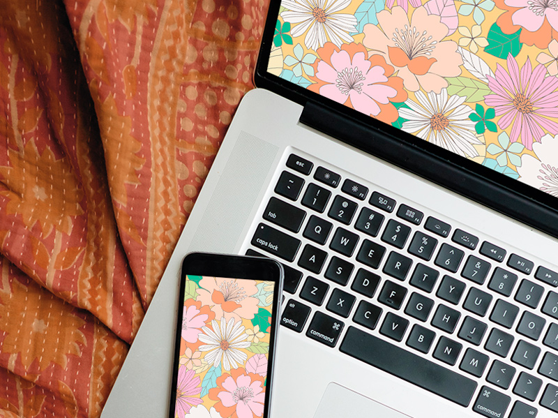 A laptop screen displaying the free July downloadable desktop wallpaper, with a mobile phone displaying the free downloadable mobile wallpaper lying nearby.