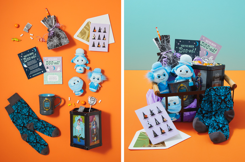 A Disney The Haunted Mansion themed boo bag kit with a trio of Hitchhiking Ghosts itty bittys plush, a Folish Mortals mug, Damask Wallpaper Socks and Haunted Portrait Candy Bowl are placed in a black, open-weave metal basket with wooden handles, and accompanied by a card with paper craft witch hats on the front and a treat bag with a colored pencil sticking out the top of it, tied up to look like a witch's broom; the final touch is a free printable that explains to the recipient that they've been