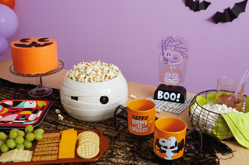 A table set for a Snoopy Halloween party is set with orange mugs that feature Vampire Snoopy and Woodstock, and read,