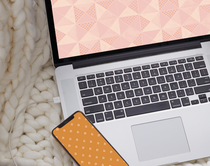 A laptop displaying the November digital wallpaper sits on cream-colored, chunky knit, woven blanket; on its keyboard lays a smartphone that displays the mobile size of the November digital wallpaper.